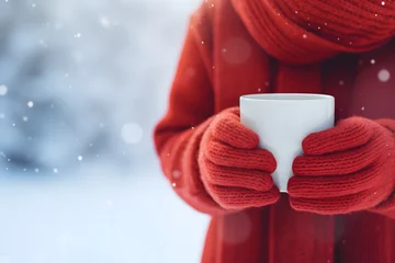 Fotobehang Person with red mittens, coat and scarf holding white mug with coffee or cocoa in front of snow winter landscape © Firn