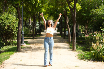 Obraz premium Beautiful Spanish brunette woman with long curly hair raises her arms to the blue sky. The woman is happy and thanks god and life for every day. Concept happiness and thankfulness.