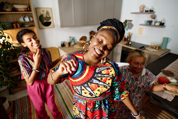 Young cheerful woman in national dress performing dance in front of camera against her two excited daughters dancing with her