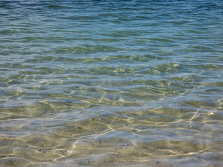 Crystal clear transparent water in shades of blue and turquoise with fine white sand base with bright reflection of sun in water movement
