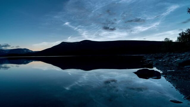 Timelapse of noctilucent clouds reflecting in the clear lake. Mystic, extraterrestial mood. Filmed after sundown in the mountains in Norway, Scandinavia.