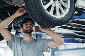 Fototapeta premium Caucasian car mechanic replace tyre on wheel at auto garage shop. Technician worker checking after service for safety transportation.