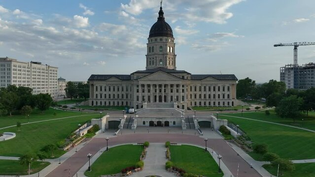 Kansas state capitol building standing tall in downtown Topeka, KS. Aerial push in shot over capitol grounds on beautiful summer day during sunset.