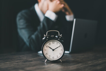 A clock in front of a businessman in a suit is distressed because he was fired for failing and being late. The concept of wasting time