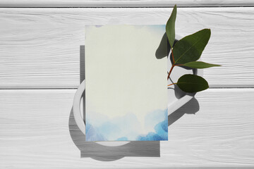 Blank invitation card and green leaves on white wooden table, top view. Space for text