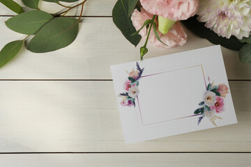 Blank invitation card, eucalyptus leaves and flowers on white wooden table, flat lay. Space for text