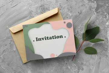 Beautiful card with word Invitation, envelope and eucalyptus leaves on grey table, flat lay