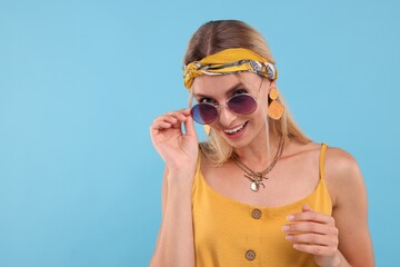 Portrait of smiling hippie woman in sunglasses on light blue background. Space for text