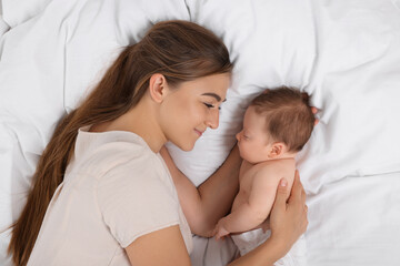 Mother and her cute newborn baby on bed, top view