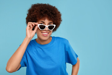 Happy young woman in stylish sunglasses on light blue background. Space for text