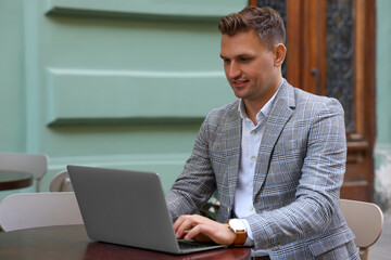Handsome man working on laptop at table in outdoor cafe