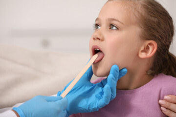 Doctor examining girl`s oral cavity with tongue depressor on blurred background, closeup. Space for text © New Africa