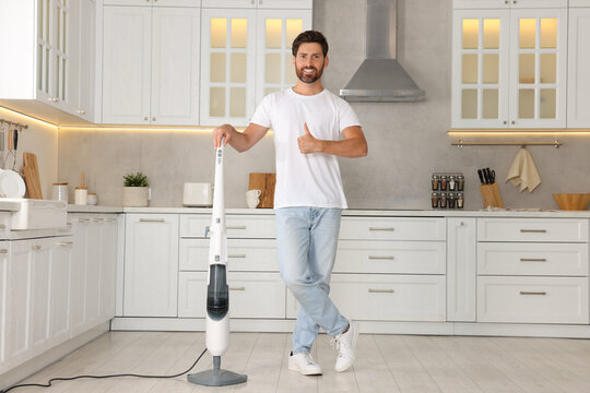 Happy man with steam mop showing thumbs-up in kitchen at home