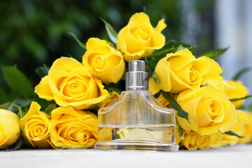 Perfume and beautiful bouquet of yellow roses on light table, closeup
