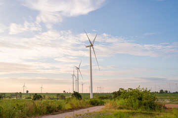 Fototapeta premium Wind turbines generate electricity in a rural area during sunset. Windmill farm on mountain with sunset sky. Wind energy, renewable energy, Green technology. 