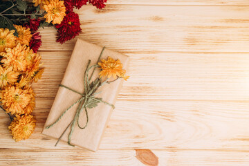 Floral background. Gift wrapped in brown paper woth yellow and red chrysanthemumsin on a light wooden background. Top view