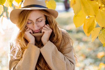 A beautiful blonde woman in a hat and coat is walking in an autumn park on a sunny day