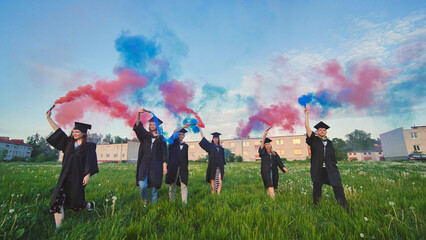 Graduates in costume walk with a smoky multi-colored smoke at sunset - obrazy, fototapety, plakaty