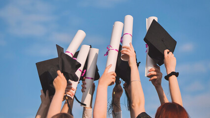 College graduates raise their hands with caps and diplomas to the sky.