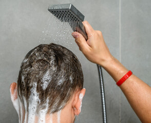 Facet spłukuje spieniony szampon do włosów pod strumieniem wody 