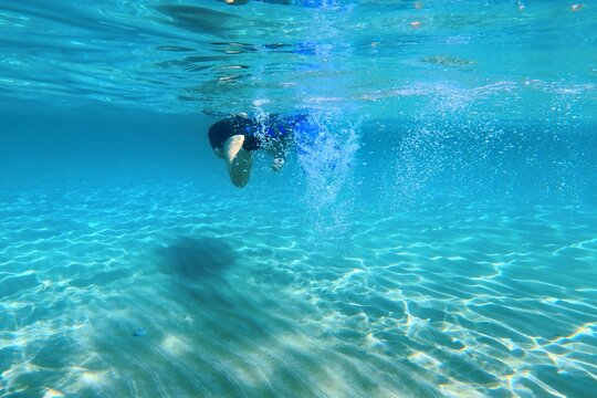 Girl snorkeling and swimming with fins in the shallow turquoise sea, sandy seabed. Crystal clear blue water with swimmer. Activity in the water, sun reflections, underwater photography.