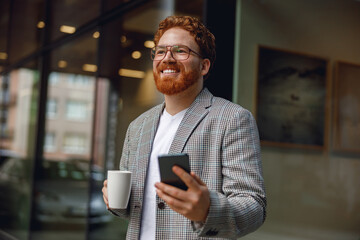 Businessman holding phone while standing near office during break time and drink coffee