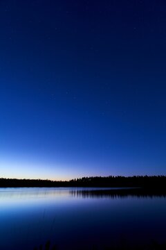 the night sky is lit up over a lake in the woods