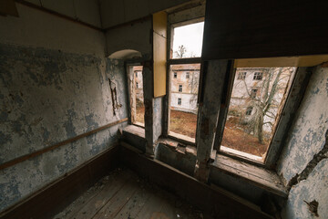 From above view of interior of room with wooden floor structure shabby unkept worn out walls peeling paint and windows overlooking, outside abandoned building with trees in daylight