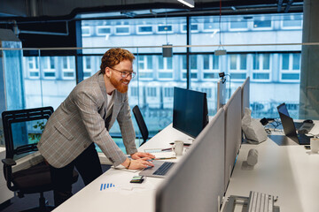 Handsome businessman working on laptop while sitting desk on office background. High quality photo