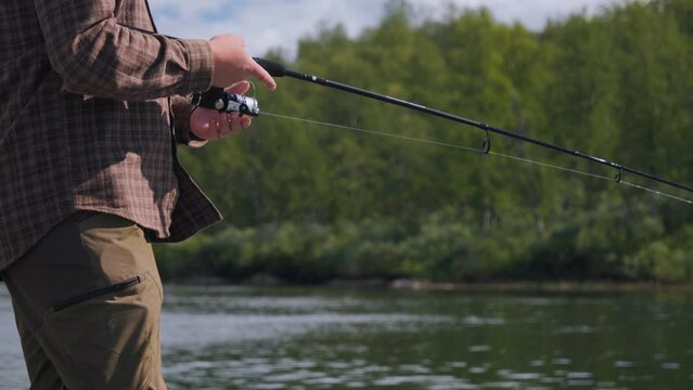 Man fishing at river, close up view of hands, techinque and casting rod. Fixed view