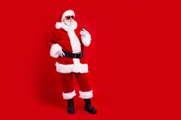 Full length photo of satisfied santa claus in sunglass look at smartphone read christmass congratulations isolated on red color background