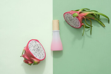 Pink bottle with wooden lid are displayed with fresh dragon fruit cut into halves. The background...