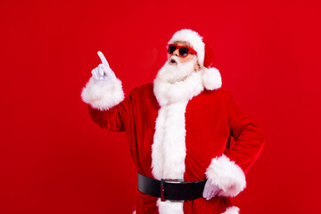 Photo of impressed astonished grandfather wear santa costume staring indicating at logo empty space isolated on red color background