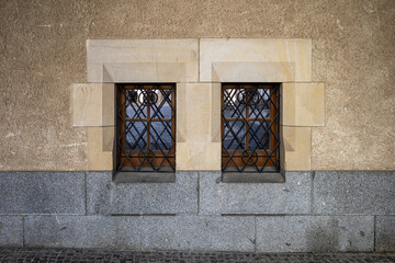 Two windows of the old building secured with bars. Windows set in a band of large stone blocks.