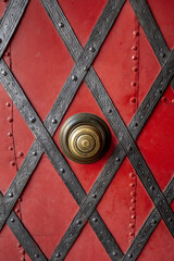 Close up of an old metal red door with diagonal iron decorative strips and rivets.