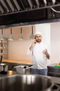 Focused caucasian male chef talking on smartphone, gesticulating in restaurant kitchen, copy space
