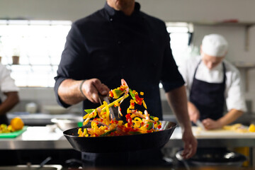 Caucasian male chef frying cutted vegetables in pan in restaurant kitchen, copy space