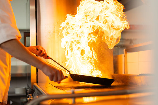 Caucasian male chef cooking with pan with fire in restaurant kitchen, copy space