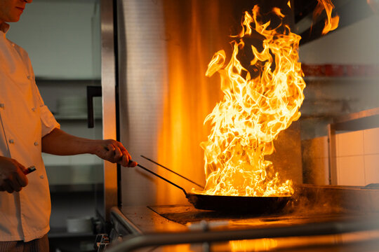 Caucasian male chef cooking with pan with fire in restaurant kitchen, copy space