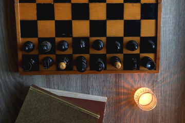 Vintage wooden chessboard, books, glasses, pen, cup of tea or coffee and scented candle on the table. Dark academia concept. Top view.