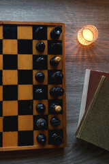 Vintage wooden chessboard, books, glasses, pen, cup of tea or coffee and scented candle on the table. Dark academia concept. Top view.