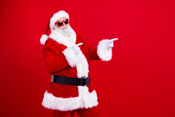 Portrait of positive santa claus indicate fingers empty space ad christmas event isolated on bright red color background