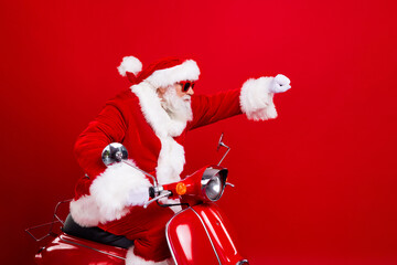 Photo of optimistic grandfather wear santa costume glasses riding on moped raising fist look empty space isolated on red color background