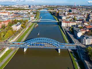 Krakow, Poland. 5 bridges on Vistula River. Aerial view. Pilsudski blue tied arc bridge with tramway and tram in front. Then footbridge and bicycle bridge. Promenades on riverbanks and tourist boats
