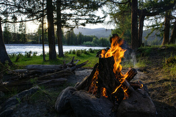 Bonfire near a mountain river. Camping by the river in the forest. The concept of adventure in the wild. Vacation concept.