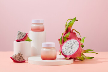 Cosmetic jars and fresh dragon fruit are placed on white podiums with a pastel background. Mockup for vegan cosmetics advertisement.