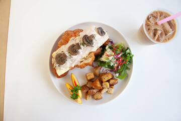 Mushroom cream cheese and scrambled egg brioche croissant sandwich with peach, rocket leaves feta cheese and sautéed potatoes with ice latte.