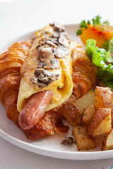 Brioche croissant egg and sausage sandwich with fresh fruits and vegetables at a cafe.
