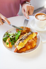 Brioche croissant egg and sausage sandwich with fresh fruits and vegetables at a cafe.