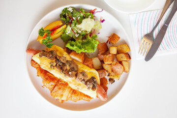 Brioche croissant egg and sausage sandwich with fresh fruits and vegetables at a cafe.